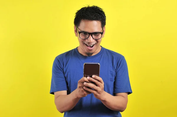 Shocked face of Asian man in blue shirt looking at phone screen — 스톡 사진