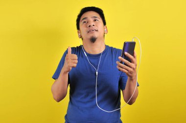 Sıradan mavi tişörtlü Asyalı adam kulaklık takıyor ve müzik dinliyor.