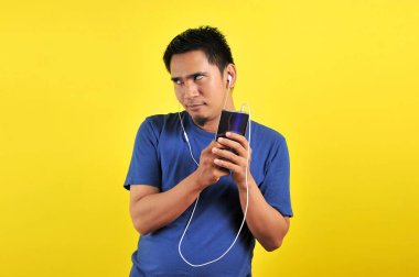 Sıradan mavi tişörtlü Asyalı adam kulaklık takıyor ve müzik dinliyor.