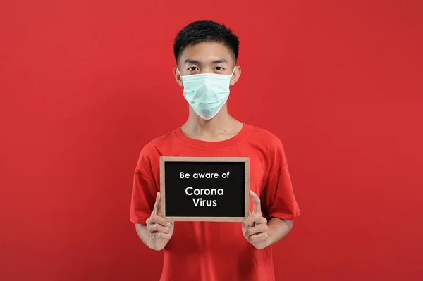 Korumalı maske takan, elinde küçük bir karatahta tutan Asyalı bir adamın portresi.