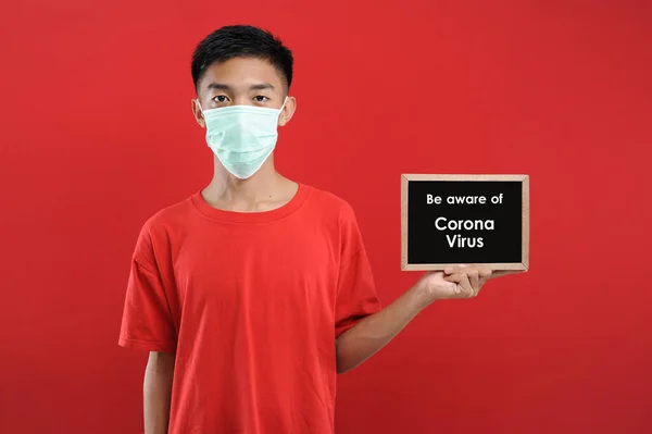 Portrét mladého asijského muže v ochranné masce, držícího malou tabuli — Stock fotografie