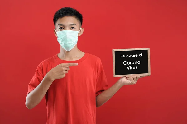 Retrato de jovem asiático vestindo máscara protetora, segurando pequeno quadro negro — Fotografia de Stock