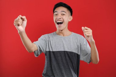 Genç Asyalı genç kazanan jest yapıyor, Happy özel bir hediye alıyor, kırmızı arka planda izole edilmiş.