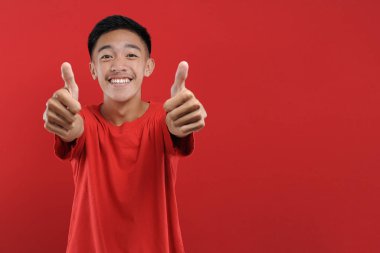 Genç Asyalı genç kazanan jest yapıyor, Happy özel bir hediye alıyor, kırmızı arka planda izole edilmiş.