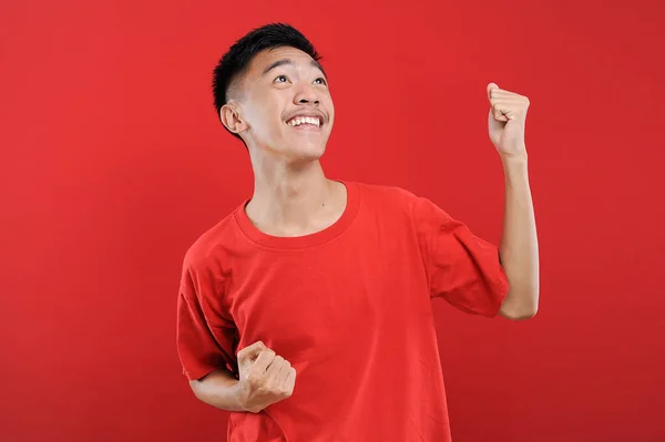 Genç Asyalı genç kazanan jest yapıyor, Happy özel bir hediye alıyor, kırmızı arka planda izole edilmiş.