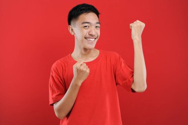 Genç Asyalı genç kazanan jest yapıyor, Happy özel bir hediye alıyor, kırmızı arka planda izole edilmiş.