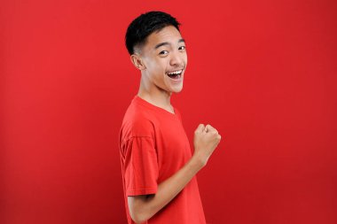 Genç Asyalı genç kazanan jest yapıyor, Happy özel bir hediye alıyor, kırmızı arka planda izole edilmiş.