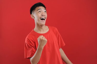 Genç Asyalı genç kazanan jest yapıyor, Happy özel bir hediye alıyor, kırmızı arka planda izole edilmiş.