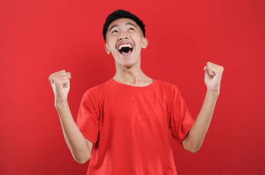 Genç Asyalı genç kazanan jest yapıyor, Happy özel bir hediye alıyor, kırmızı arka planda izole edilmiş.