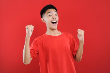 Genç Asyalı genç kazanan jest yapıyor, Happy özel bir hediye alıyor, kırmızı arka planda izole edilmiş.