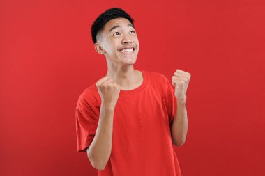 Genç Asyalı genç kazanan jest yapıyor, Happy özel bir hediye alıyor, kırmızı arka planda izole edilmiş.