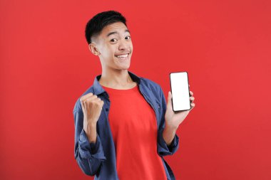 Genç Asyalı bir genç elinde cep telefonuyla fotokopi için boş bir ekran tutuyor Happy internetten özel bir hediye alıyor.