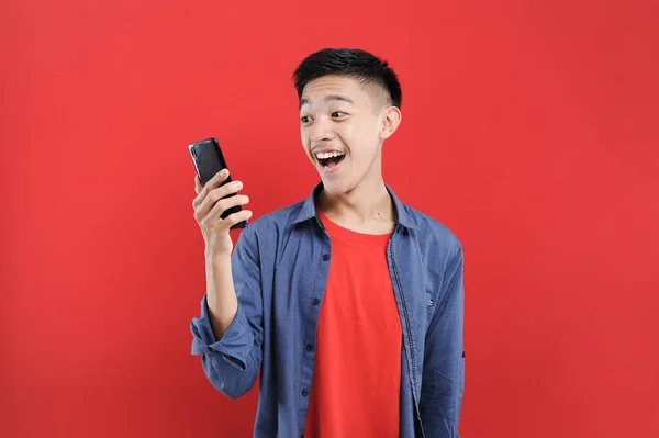 若いですアジアの10代の若者は 携帯電話を保持する勝利ジェスチャーを行います ハッピーは オンライン特別な贈り物を取得します 赤の背景に隔離 — ストック写真
