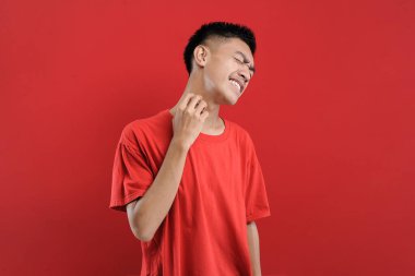 Asyalı adam kaşınıyor, derisi kaşınıyor, kırmızı arka planda izole edilmiş.