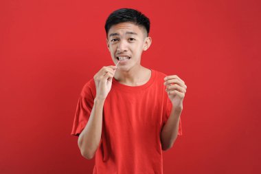 Genç Asyalı adam dişini temizlemek için kürdan kullanıyor. Sağlıklı bir hayat genç Asyalı adam. kırmızı arkaplanda izole