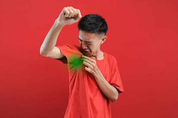 Hiperhidrozlu Asyalı bir adam koltukaltı altında terliyor, vücut konusunda kötü hissediyor, koku sorunu var, kırmızı arka planda izole edilmiş.