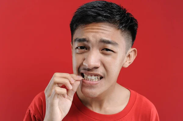 Genç Asyalı adam dişini temizlemek için kürdan kullanıyor. Sağlıklı bir hayat genç Asyalı adam. kırmızı arkaplanda izole