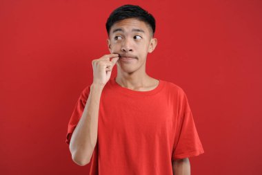 Asyalı yakışıklı adam sessizlik hareketi yapıyor. Kırmızı arkaplanda izole edilmiş. Kopya alanına bakıyor.