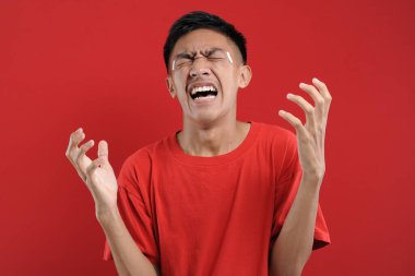 Asyalı genç adam öfkeli hareketler yapıyor. Sinirli ve duygusal. Kırmızıda soyutlanmış..