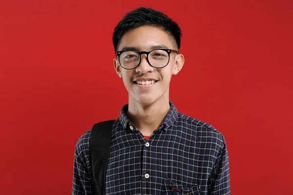 年轻的亚洲学生拿着眼镜对着相机笑 用红色背景隔离 — 图库照片