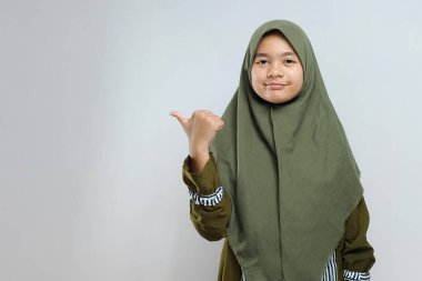 Şirin, genç, güzel Müslüman kadın fotokopi alanını işaret ediyor. Neşeli Müslüman kadın gri arka planda kopya alanını işaret ediyor.