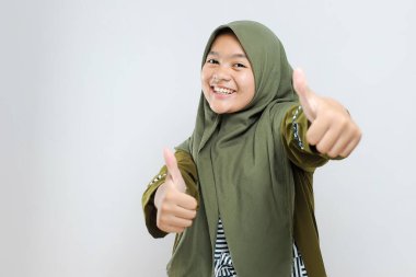 Müslüman tesettürlü genç bir kız elinle olumlu jest yapmayı onaylıyor, gülümsüyor ve başarı için mutlu. Kazanan jest.