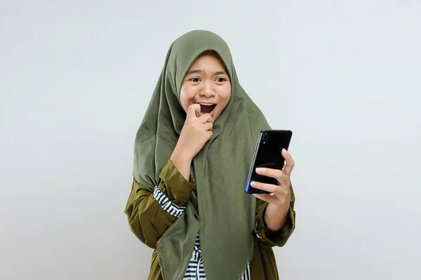 兴奋的年轻亚洲穆斯林女性震惊地看着智能手机 得到了最好的礼物 优惠券 与灰色隔离 — 图库照片
