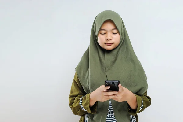 若い美しいアジアのイスラム教徒の女性が携帯電話の画面を見て 灰色で隔離された — ストック写真