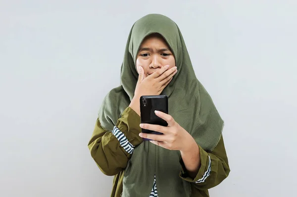若いアジア系ムスリム女性は携帯電話で悪いニュースを読みました ポートレート 若いイスラム教徒の女性の叫びは 携帯電話で見ます グレーに分離 — ストック写真
