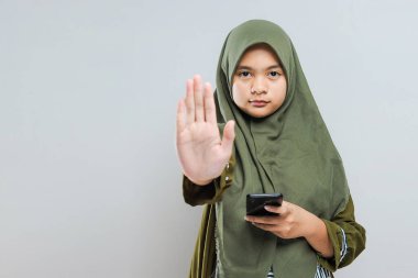 Elinde cep telefonu olan genç Müslüman bir kadın. Gri üzerine izole edilmiş zorbalık hareketini durdurdu.