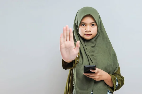 Молодая Мусульманка Держит Мобильный Телефон Жестом Остановки Запугивания Изолированный Сером — стоковое фото