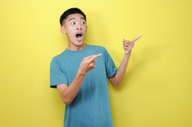 Sarı arkaplanda izole edilmiş fotokopi alanını işaret eden yakışıklı Asyalı adamın portresi.