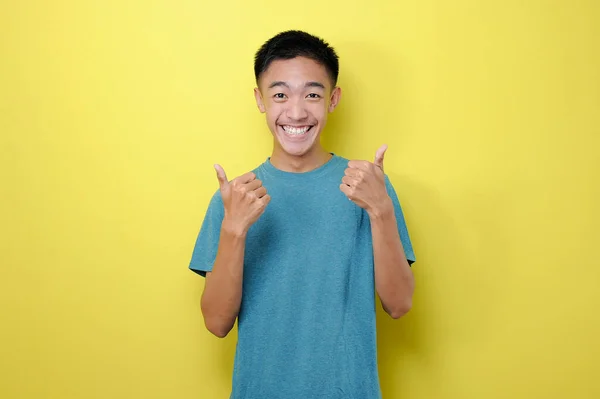 幸せな若いアジアの男が興奮し 黄色の背景に隔離された2本の親指をあげる — ストック写真
