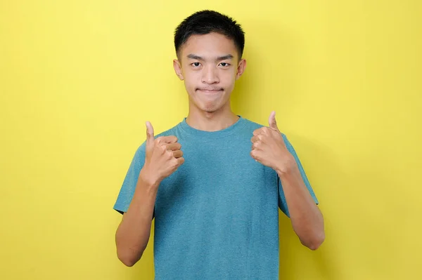 アジア系の若者が口を閉じて親指を2本上げ黄色の背景に隔離された — ストック写真
