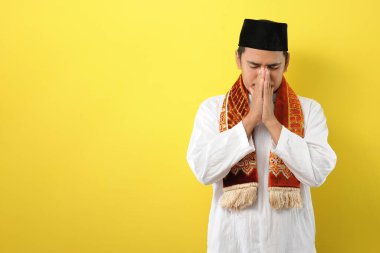 Genç Asyalı Müslüman adam elleriyle yüzünü kapattığı için üzgün hissediyor. Alan kavramını kopyala, sarı arkaplanda izole edilmiş