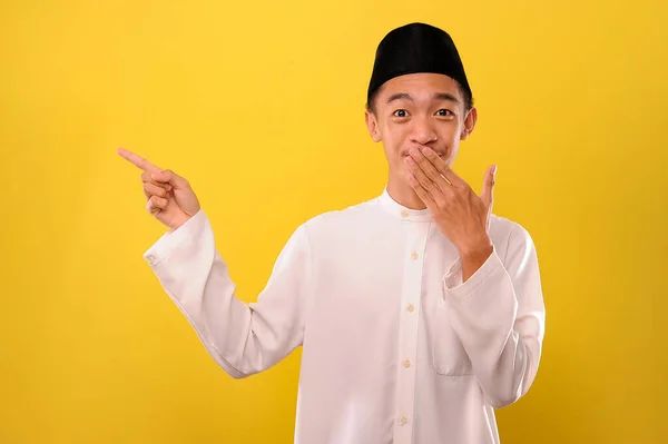 黄色の背景の上に隔離された驚きと指差しの指を表明面白い若いアジアのイスラム教徒の男のイメージ — ストック写真