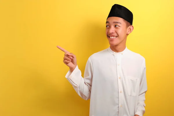 黄色の背景に隔離された何かを提示するコピースペースを示すことを指す幸せな若いアジアのイスラム教徒の男 — ストック写真