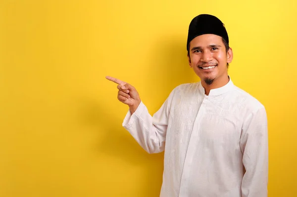 黄色の背景に隔離された何かを提示するコピースペースを示すことを指す幸せな若いアジアのイスラム教徒の男 — ストック写真