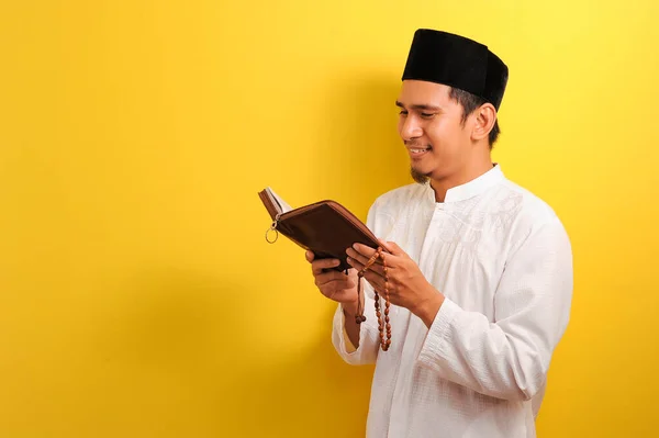 Kuran okuyan Asyalı genç Müslüman adamın portresi, sarı arka planda izole edilmiş.