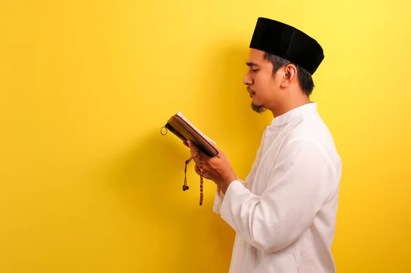 黄色の背景に隔離されたクルアーンを読む若いアジア系ムスリム男性の肖像 — ストック写真