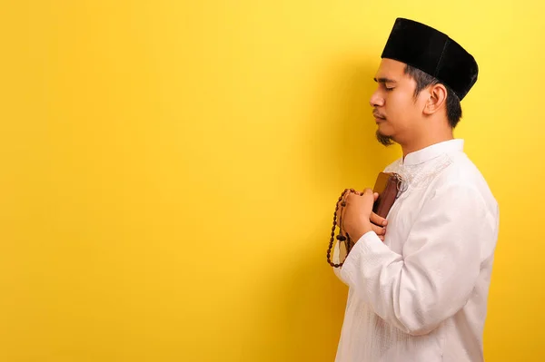 クルアーンを保持する平和的な若いアジアのムスリム男性の肖像画と黄色の背景に隔離されたコピースペースを持つ祈りのビーズ — ストック写真