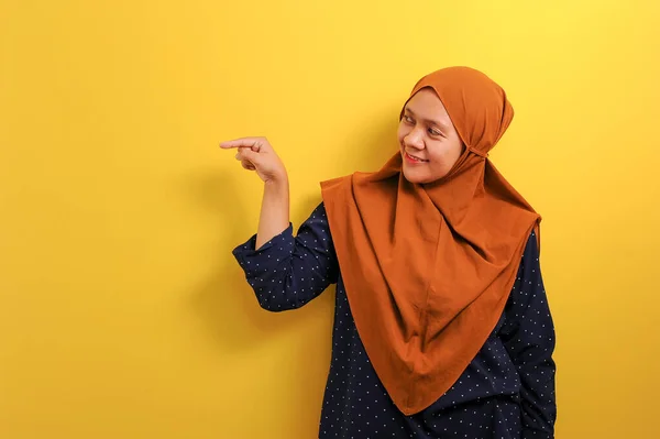 黄色の背景に隔離された何かを提示するコピースペースを示すことを指す幸せな若いアジアのイスラム教徒の女性 — ストック写真