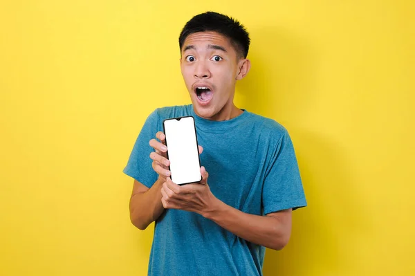 Genç Asyalı adam, sarı arka planda izole edilmiş beyaz telefon ekranını kameraya gösteriyor.