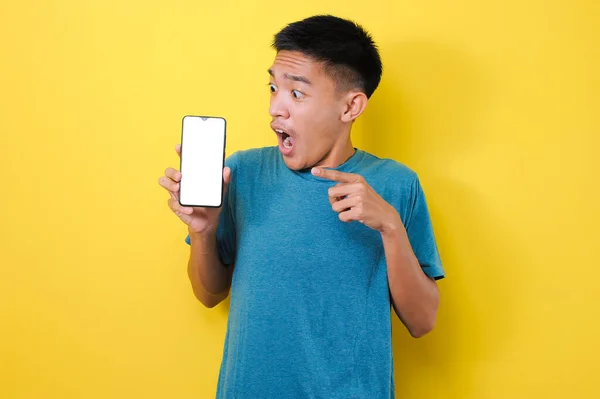 兴奋的亚洲年轻人震惊地将手机屏幕对准了白色手机屏幕 被黄色背景隔离 — 图库照片