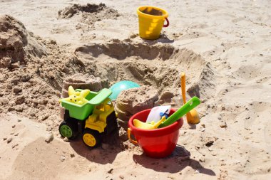 Çocukların plastik oyuncakları yeşil uçlu sarı araba, kürek, sarı ve kırmızı kovalar, sahilde sarı kumlu yeşil top. Güneşli bir günde çocukların kumsaldaki oyuncakları. Oyun parkında kum havuzu