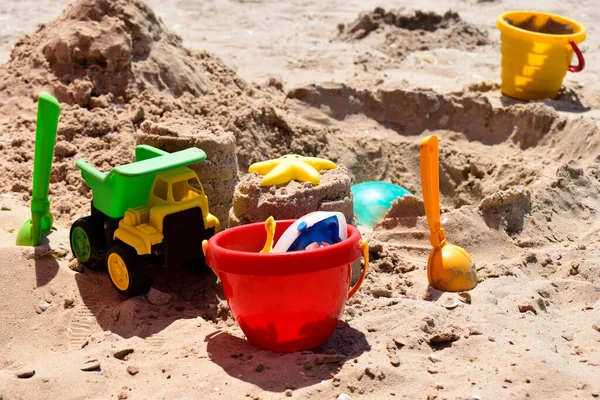 Children\'s plastic toys green end yellow car, shovel, yellow and red buckets, green ball with yellow sand on the beach by sea. Children\'s beach toys on sand on a sunny day. Sandbox on the playground