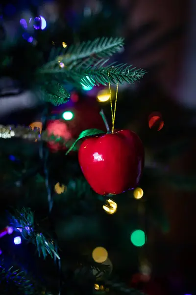 Bola roja de navidad en forma de manzana colgando de un árbol de navidad con luces borrosas en el fondo — Foto de Stock