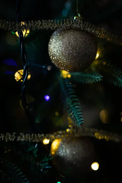Bola de natal dourada brilhante pendurada em uma árvore de natal com luzes embaçadas no fundo — Fotografia de Stock