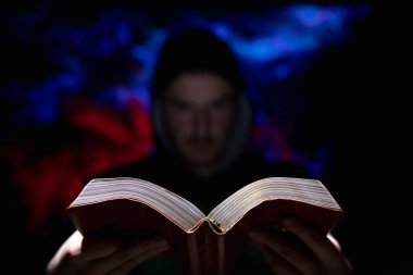 Karanlık arka planda bulanık bir adam elinde dini bir kitap tutuyor.