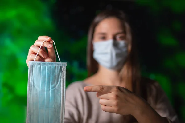 Woman with face mask holding a face mask inviting others to use one on green background safety concept corona virus